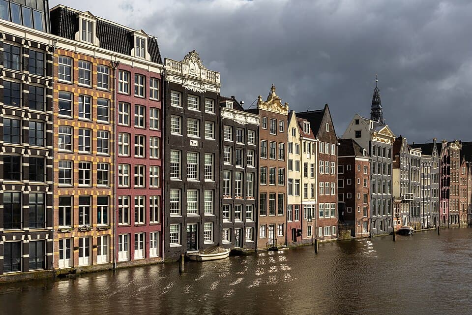 Colorful canal houses along Damrak in Amsterdam under a dramatic cloudy sky