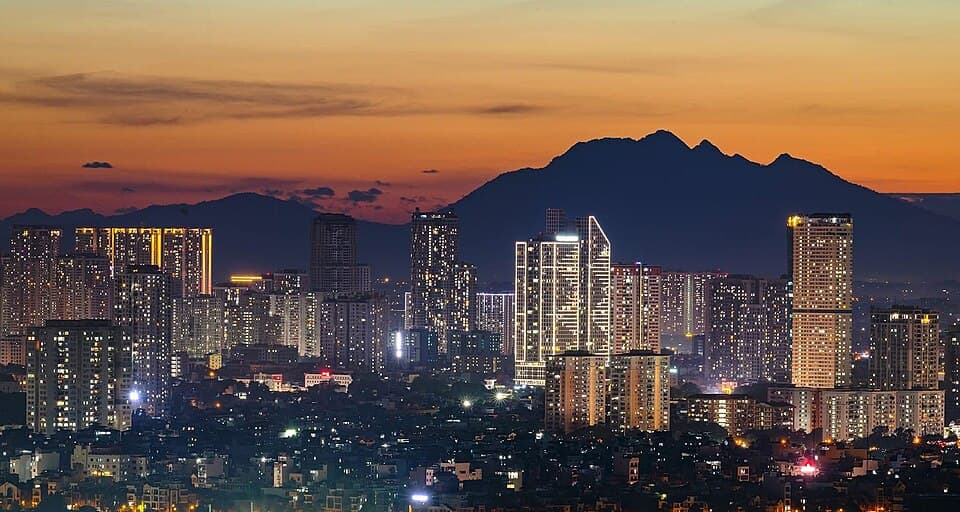 The illuminated Hanoi skyline beneath Ba Vi Mountain at sunset